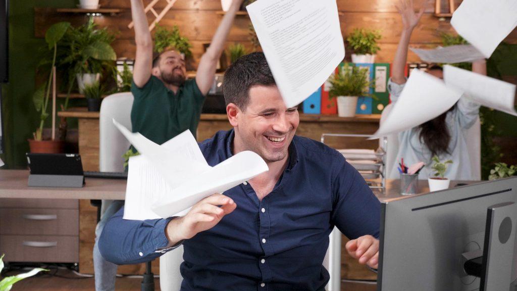 Des hommes d'affaires heureux et prospères lancent des documents de marketing en l'air après avoir terminé un projet de gestion et célèbrent la promotion de l'équipe dans un bureau de startup. Une équipe d'hommes d'affaires enthousiaste qui profite d'une victoire commerciale.